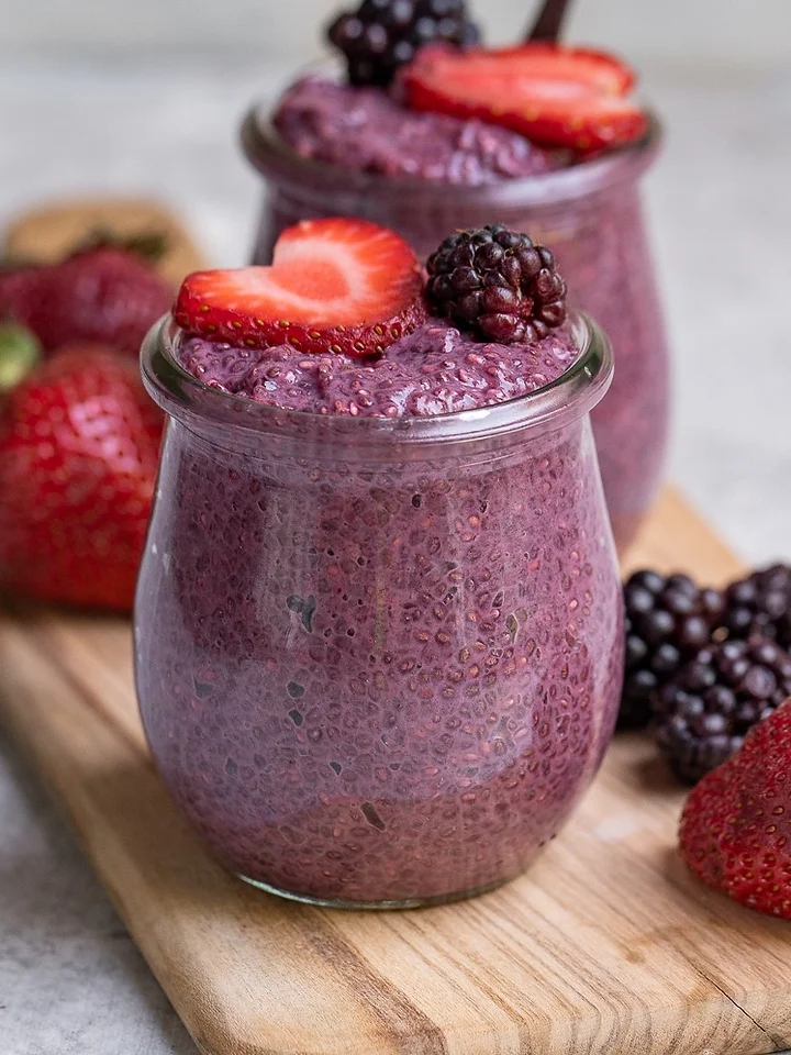 Two glasses filled with berry chia pudding and some fresh berries on a wooden board