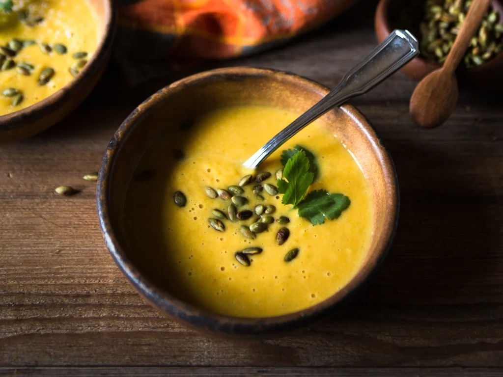 A bowl of carrot soup with some garnish on a wooden counter