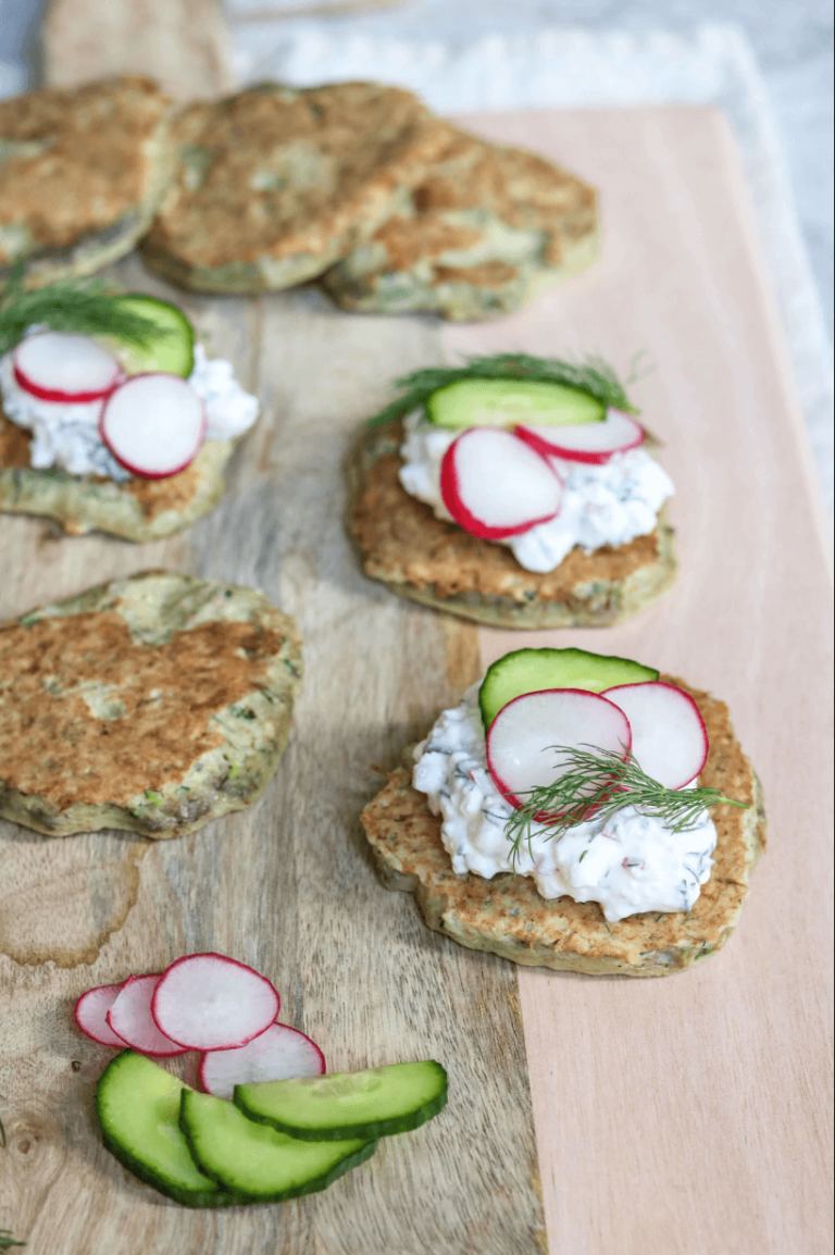 Potato cakes topped with cottage cheese, cucumber and radish on a wooden board